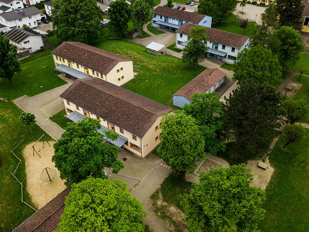 Luftaufnahme eines Wohnviertels mit mehreren Mehrfamilienhäusern, umgeben von Bäumen und Grünflächen.