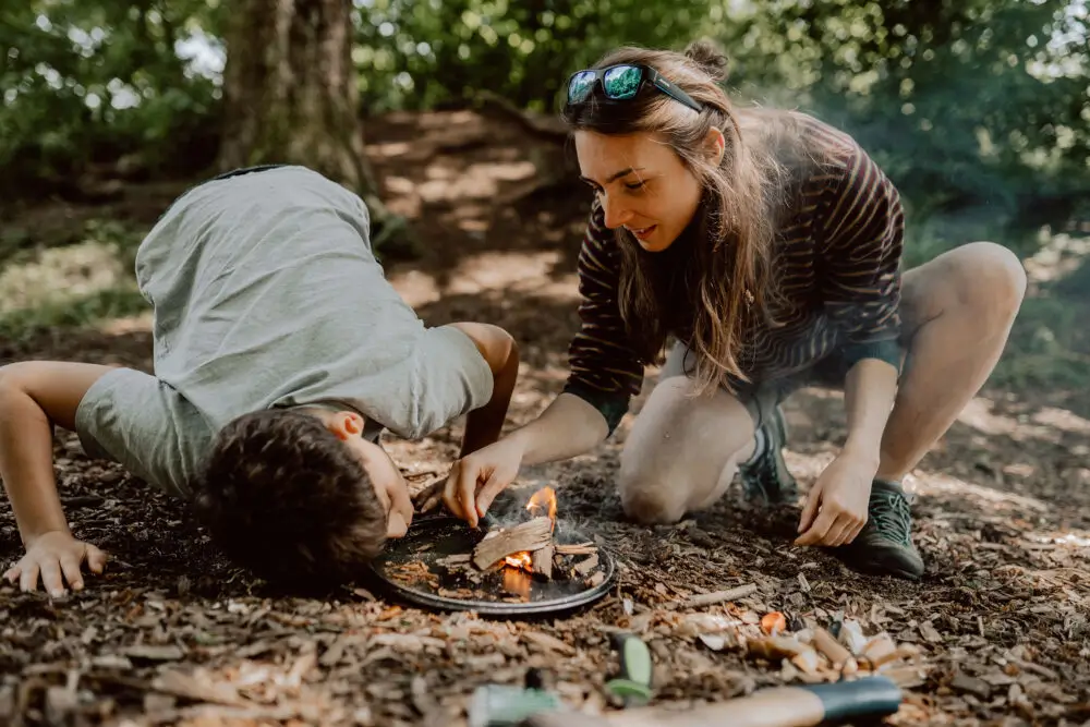 Eine Frau und ein Kind zünden im Wald ein kleines Lagerfeuer an.