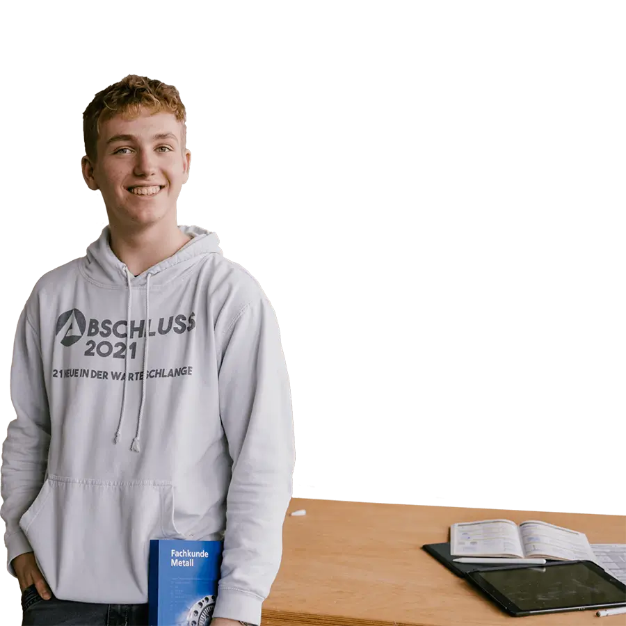 Jugendlicher mit weißem Hoodie und Buch "Fachkunde Metall" steht in einem Klassenraum neben einem Tisch mit offenen Büchern und Tablet.