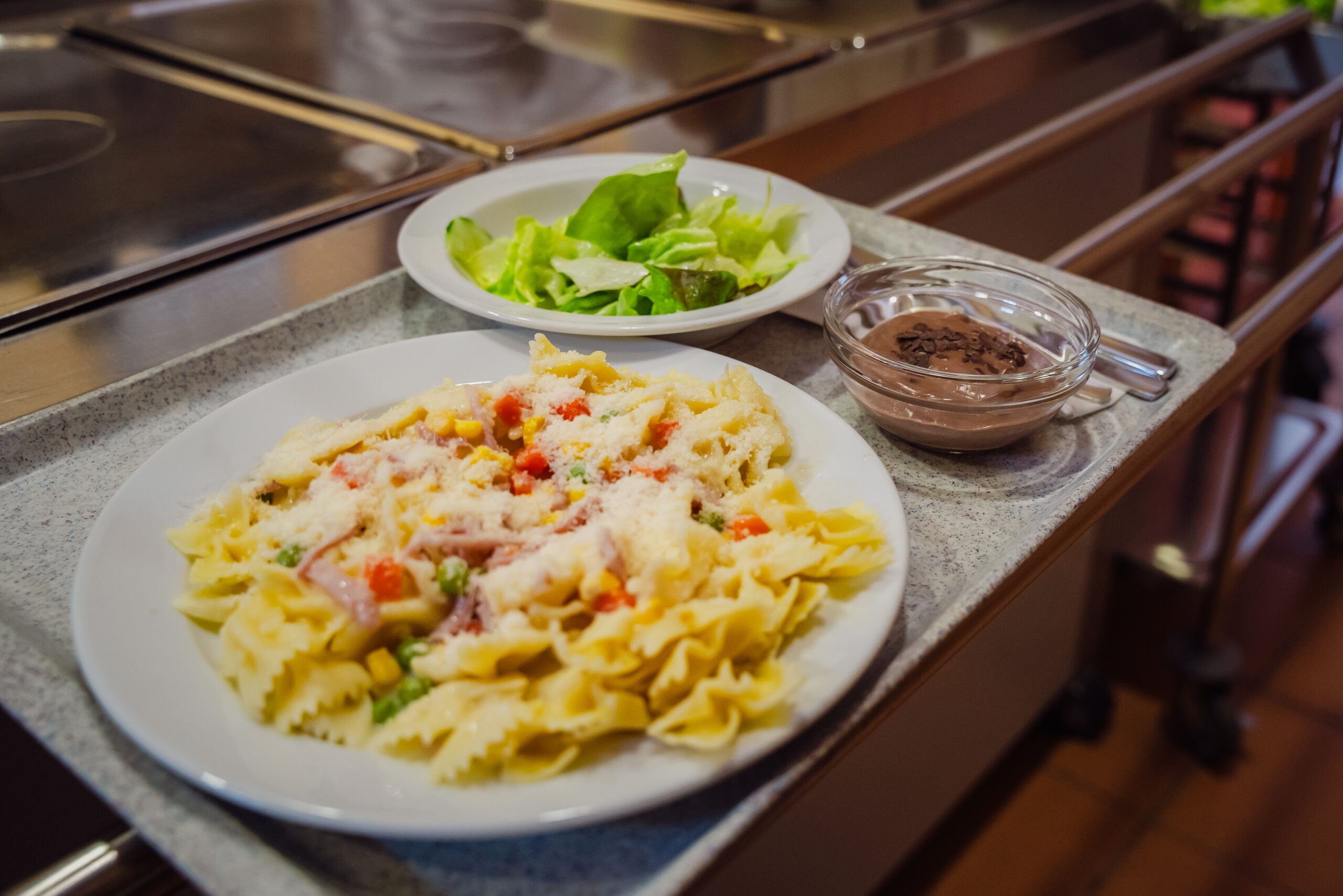 Ein Teller mit Pasta, eine Schüssel mit Schokoladensoße und ein kleiner Salat auf einem Speiseteller.