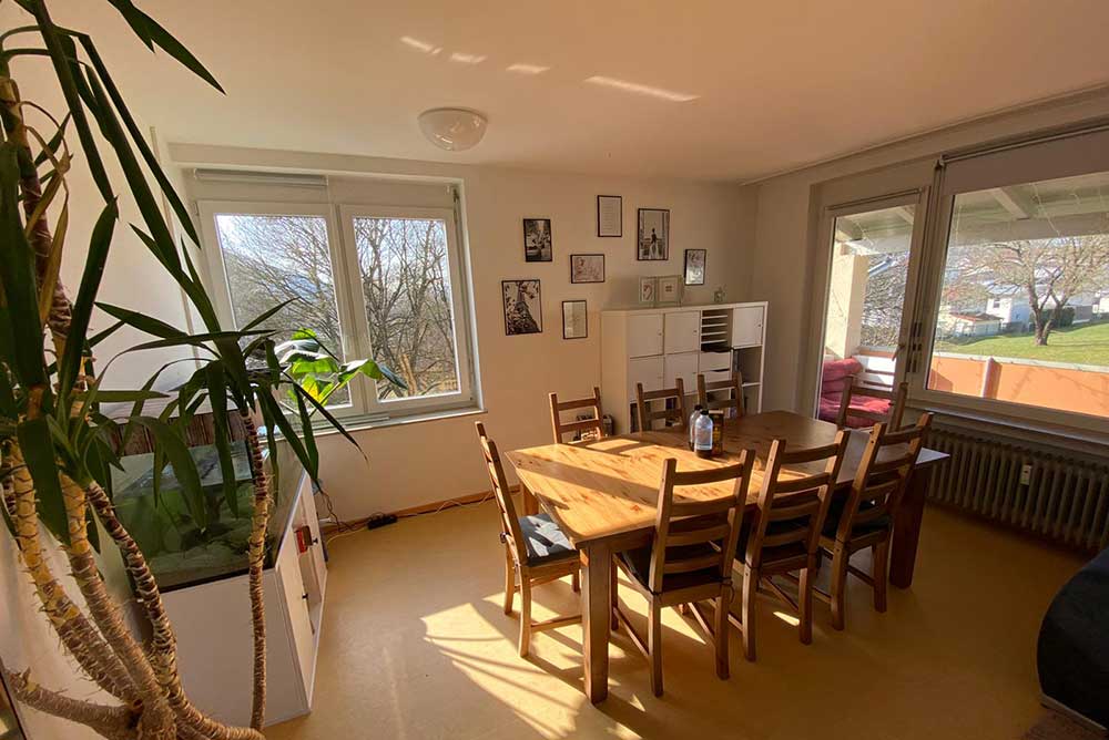 Heller Esszimmerraum mit einem großen Holztisch, acht Stühlen, großen Fenstern,