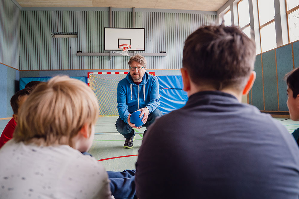 Ein Trainer spricht mit einer Gruppe von Kindern im Turnraum