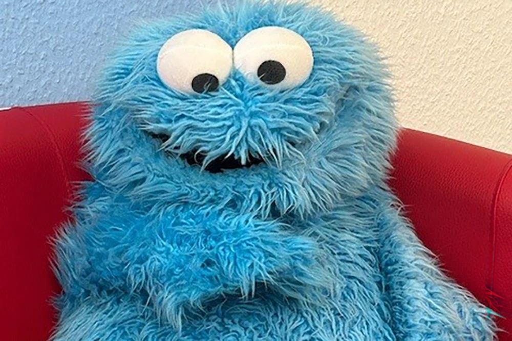 Blaues flauschiges Monster mit großen Augen sitzt auf roter Couch.