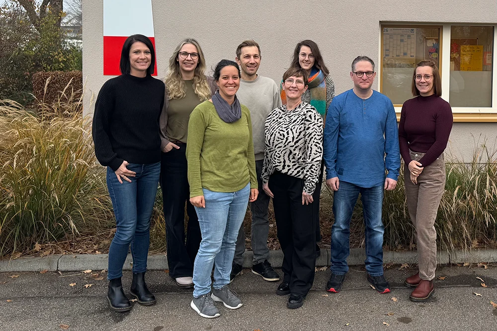 Eine Gruppe von Menschen posiert draußen vor einem Bürogebäude.