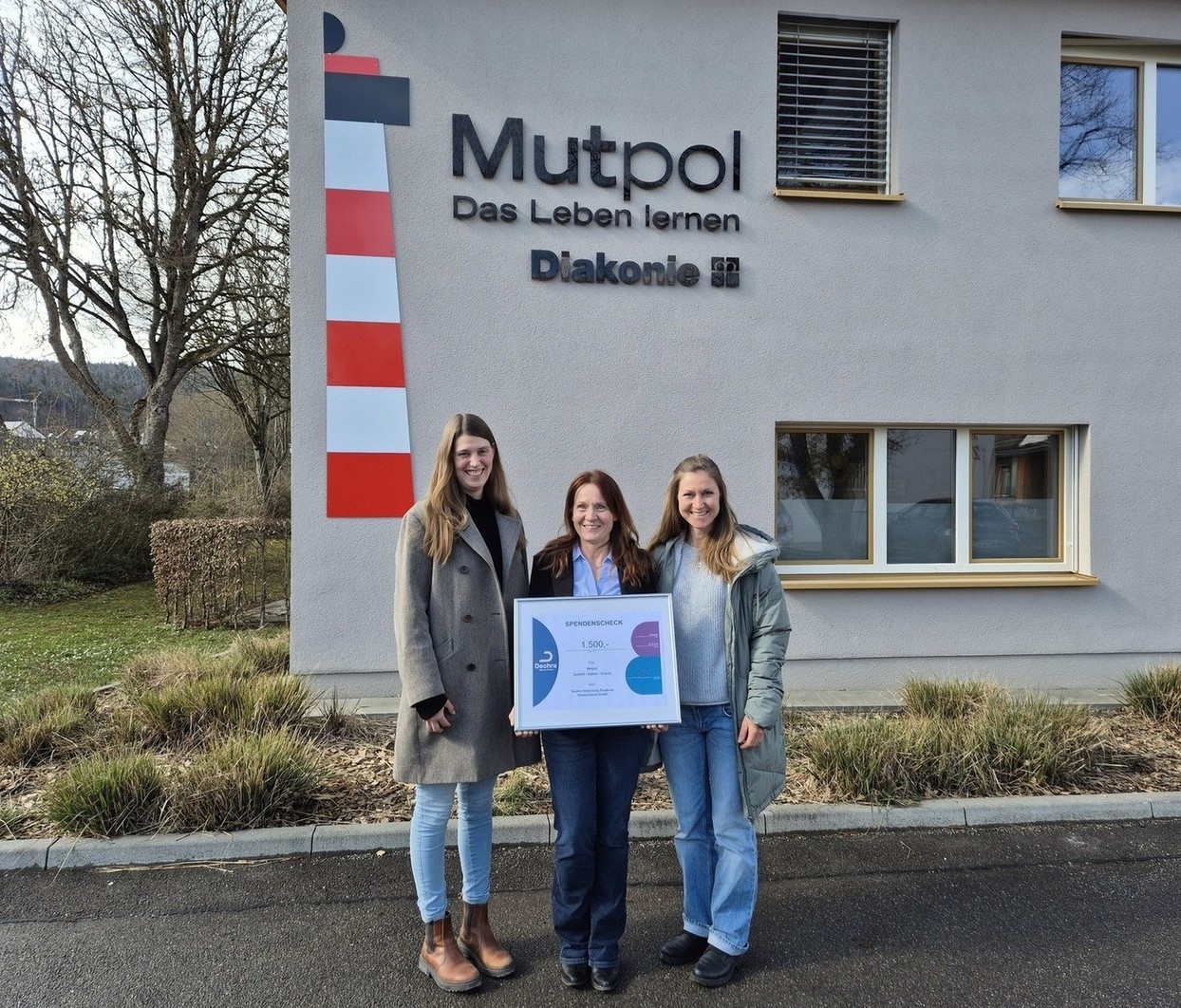 Drei Frauen halten einen Spendencheck vor dem Mutpol-Diakonie-Gebäude.